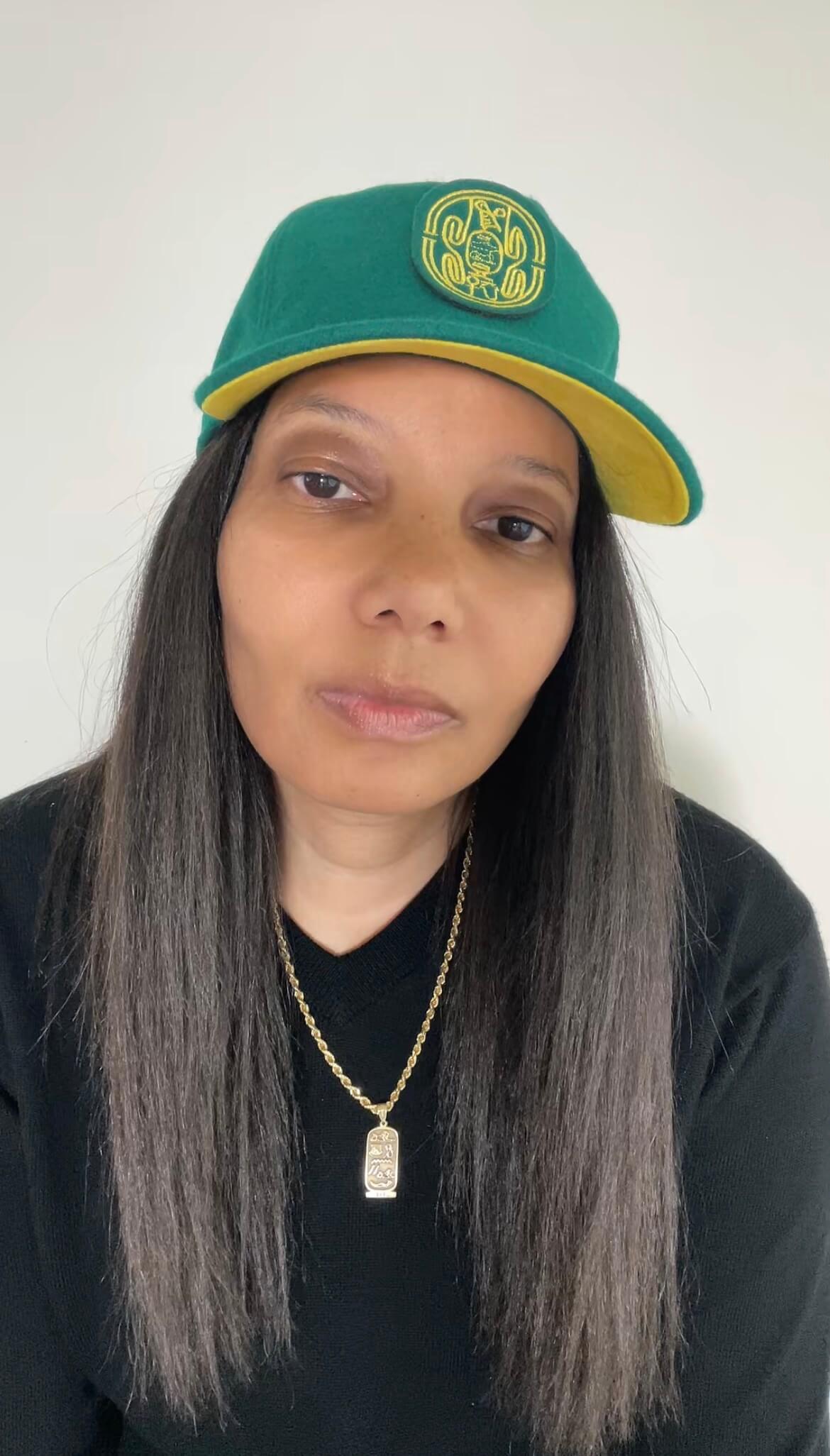 A woman with long dark hair wearing the Origins hat in emerald and citrine.