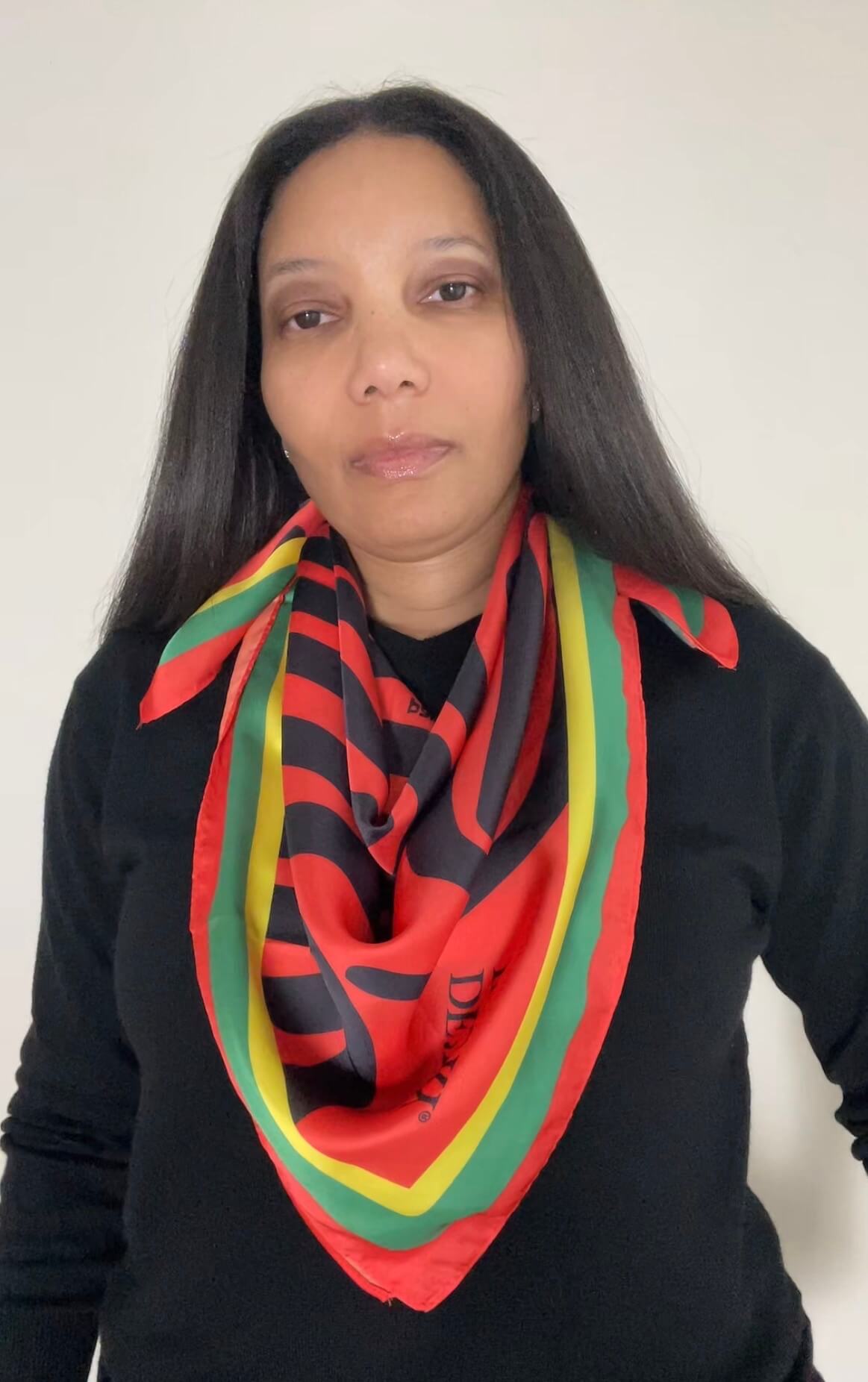 A woman with long black hair wearing a black long-sleeve top and the Scarab Journey scarf in deep amber, citrine, black and emerald.