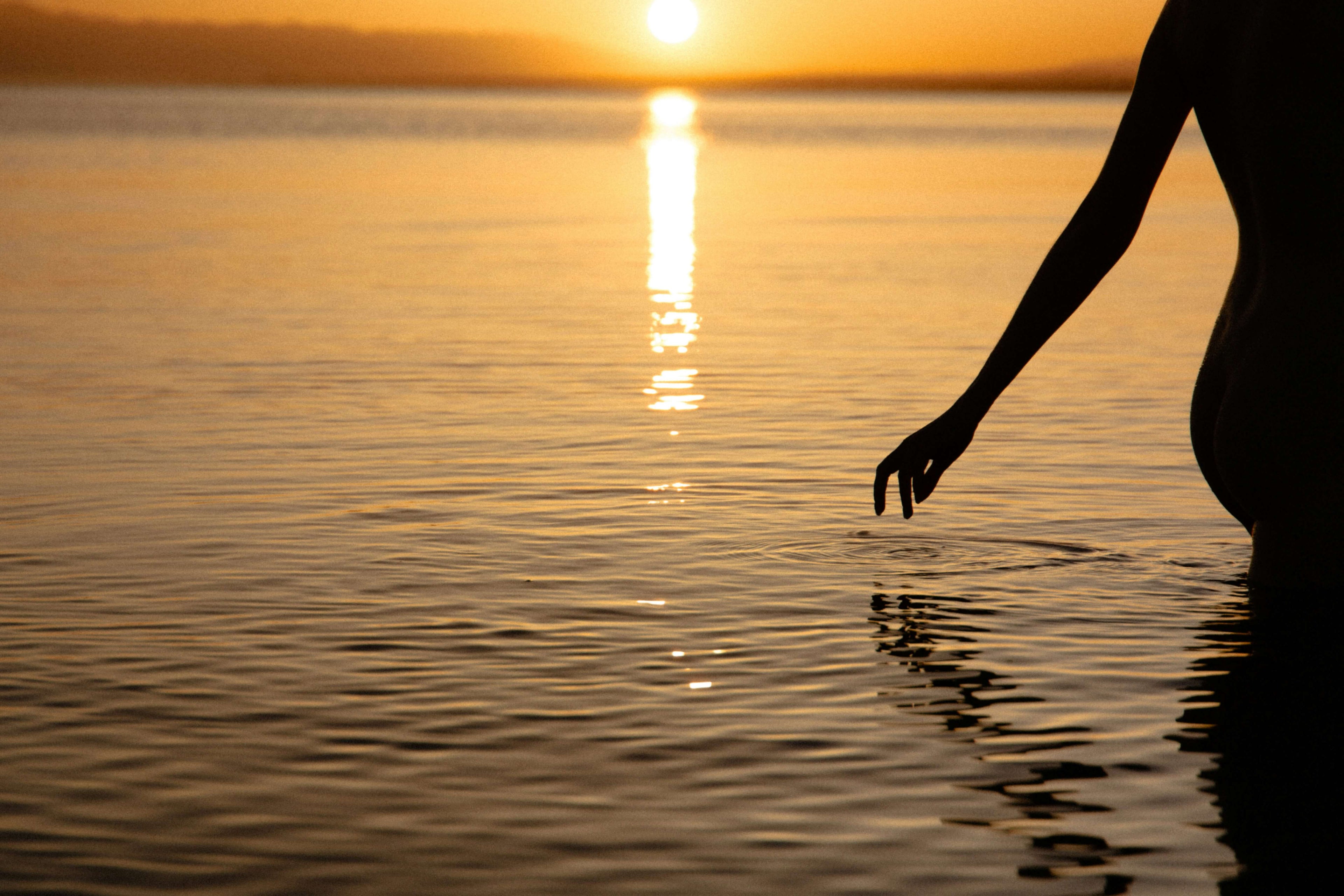 Person touching water at sunset with golden light reflecting on the water surface